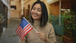 © Krakenimages.com - Woman with asian descent holding american flag on city street smiling outdoors in usa, representing cultural diversity and patriotism in urban setting.