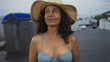 © Krakenimages.com - Woman in bikini and sunhat standing near outdoor recycling container on a sunny street.