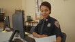© Krakenimages.com - Woman officer in uniform works at desk in police station, engaging with paperwork on computer, showcasing a professional setting with focus on law enforcement responsibilities.