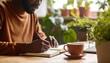 © David Andres - Persona escribiendo en su diario personal, taza de té al lado, escritorio de madera, plantas alrededor, estilo cálido y acogedor