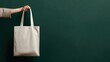 © IUYIU - Fashionable Female hands holding an Oatmeal white blank tote bag mock up, standing in front of flat dark green wall with soft lighting