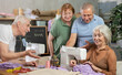 © JackF - Enthusiastic older adults, women and men, gathering around sewing machine in training workshop while female seamstress explaining stitching techniques and fabric positioning, sharing professional tips