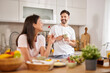 © Stockphotodirectors - A couple is seen in their bright kitchen, smiling and chatting as they enjoy a light breakfast with drinks and fresh produce on the counter, creating a cheerful atmosphere.