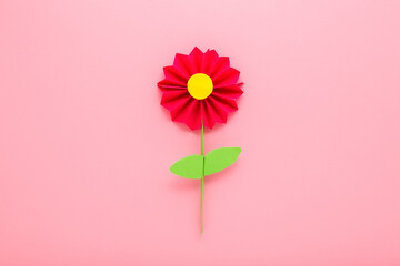 Wall Mural - Flower with green leaves from colorful application paper on light pink table background. Pastel color. Closeup. Top down view.