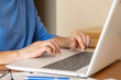 © Nanci - Businesswoman wearing a blue shirt is carefully typing on a laptop keyboard, developing a financial plan in her home office, surrounded by paperwork and glasses