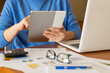 © Nanci - Businesswoman using digital tablet is analyzing financial charts, data, and investment plan with laptop, calculator, and eyeglasses on the desk, developing a successful business strategy