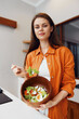 © SHOTPRIME STUDIO - Young woman holding a bowl of fresh salad in a bright kitchen, showcasing healthy eating habits and vibrant colors with a joyful expression