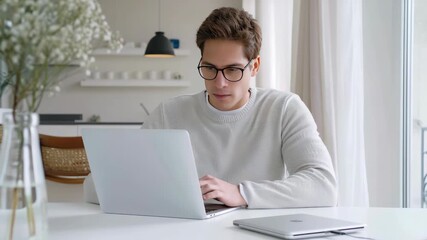 Poster - A young man concentrates on his laptop, surrounded by a minimalistic and inviting workspace enhanced by natural light