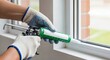 ©  S u n n y B u n n y - A person in gloves uses a caulking gun to apply sealant to a window frame. Home improvement, repair, and installation concept.