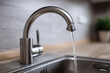 © Sabana - Close up of a silver faucet with water running into a stainless steel sink bowl
