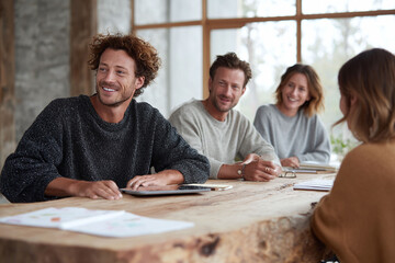 Poster - Inspiring teamwork Group of smiling professionals collaborating around a rustic table, illuminated by natural light. Perfect for depicting innovation and positive work culture.