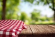 © Shelley - Red and white checkered tablecloth on a wooden board, set against a blurred green park background, ideal for summer picnic and product display montages.