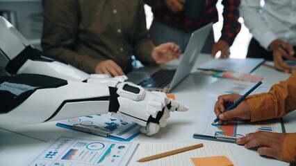 Poster - In a modern office setting, a robot arm collaborates with human participants during a meeting to analyze data, featuring charts and documents that showcase innovative strategies.Noogenesis