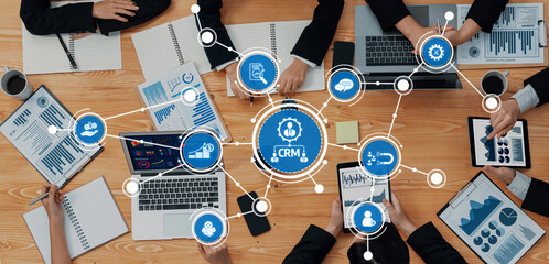 Poster - A dynamic business meeting showcasing professionals collaborating around a table with CRM visuals and data reports, highlighting teamwork and modern technology solutions. Amity