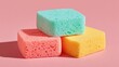 © Kristina - Three vibrant kitchen sponges in mint green, coral pink, and yellow are stacked together on a pastel pink surface.