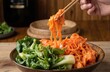 © Pete - Enjoy close-up of Korean kimchi bok choy, homemade fermented dish, with chopsticks lifting noodles. Served in wooden bowl with fresh green vegetables on rustic table, vibrant meal represents healthy
