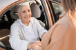 © Pixel-Shot - Young caregiver helping senior woman to stand up from car outdoors