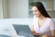 © PheelingsMedia - Happy woman using laptop on a couch at home