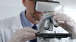 © rogerphoto - Close up of scientific researcher wearing white protective gloves carefully calibrating laboratory microscope, performing precision medical investigation. Medicine and science concept