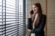 © Apichat - Businesswoman making a phone call near window with blinds in office