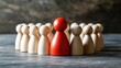 © Worrapol - Wooden figures depicting leadership and teamwork with a single red figure standing out among a circle of neutral-colored figures on a textured background
