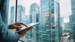 © CStock - A businessman using a tablet while looking at urban skyscrapers through a window in a modern office.