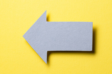 Poster - Gray cut out blank paper cardboard arrow direction sign with copy space for text on yellow background, flat lay top view pointing symbol conceptual message backdrop
