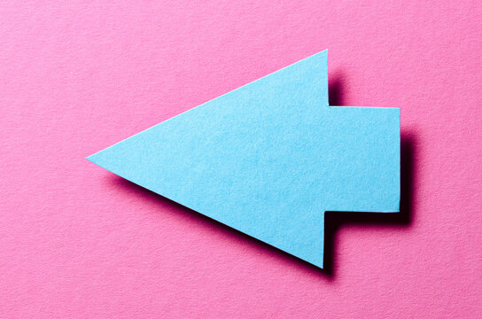 Blue cut out blank paper cardboard arrow direction sign with copy space for text on pink background, flat lay top view pointing symbol conceptual message backdrop