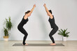 © TRAVELARIUM - Two adult women practice yoga together in minimalist room. Dressed in black activewear, they are positioned on yoga mat, engaging in focused physical exercise