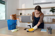 © Natee Meepian - Home Cleaning. Young woman happily organizing her workspace while cleaning.