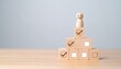 © Innovative - Wooden figure standing atop pyramid of blocks with icons—symbol of achievement, goal mastery