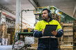 © Koldo_Studio - Supervisor wearing ear protection and high visibility jacket writing notes on clipboard in a wooden pallet recycling factory