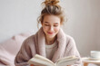 © arko - young woman wrapped in soft cozy blanket immersed in good book on comfortable couch