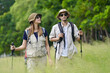 © Nassorn - Tourist couple hiking walking together over grassland of the plains. Active multiracial woman trekking through nature grass field over lowland in rural trail. Portrait of people in peaceful meadow.