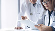 © tippapatt - Two asian doctors discuss diagnosis, analyzing data on digital tablet in hospital office. Male and female medical professionals have a patient case conference at doctor's office, close up