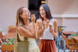 © we.bond.creations - Two cheerful female friends enjoying ice cream cones together on a sunny day, laughing and having fun