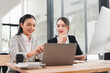 © PRIME STOCK LAB - Two Asian businesswomen working together at modern office desk, discussing project on laptop with documents, coffee cup, and digital tablet, showing teamwork and focus