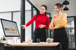 © kenchiro168 - Two Asian businesswomen in modern office discussing data analysis on computer screen, smiling and collaborating on project, teamwork and professional environment