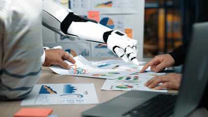 Poster - A human and a robotic hand collaborate over data analysis papers, displaying vibrant graphs and charts in a contemporary office setup, symbolizing innovation and integration.Noogenesis