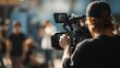 © SaroStock - Person using a professional video camera to film a scene with blurred people in the background during the day in an outdoor urban setting