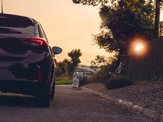 Wall Mural - A black car is parked in front of a white building. The car is dark and has a red light glowing on the back. The sunset scene is quiet and peaceful. Coming back home late after work theme