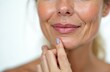 © Viktor - Close-up of mature woman mouth and chin area revealing prominent wrinkles and nasolabial folds. Skin texture shows signs of aging. Thoughtful gesture as finger touches chin, highlighting facial aging.