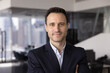 © fizkes - Head shot close up portrait of professional man dressed in formal jacket posing in city office, stare at camera with confident and contented expression. Career growth, human resources, achievements