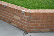 © Trevor Cook - Short red brick retaining wall. Crack in brick sealed with filler. Green grass on other side. Anti skateboard brackets installed.