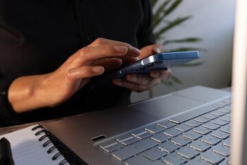 Poster - Close-up of the hands of a businesswoman sitting in front of her computer while holding a cell phone