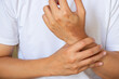 © Prasert - Asian man holding wrist in pain from daily chores, seated indoors ideal for medical ads on wrist strain, tendonitis, or repetitive stress injury.