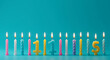 © Jamil - Collection of lit birthday candles in various colors and numbers on a teal background
