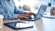 © NafiliaEmil - A businesswoman types on a laptop keyboard while a digital tablet with a reflection of her hand is on an office table, representing online work and remote employment.