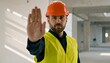 © photostockatinat - A construction worker signaling stop on a building site, looking directly at the viewer, his outstretched hand a clear symbol of warning
