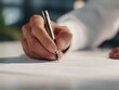 © Wang - A hand holding a pen writes on a white paper.